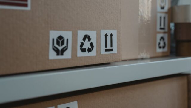 A modern warehouse packing line with branded sustainable paper boxes and bags overlaid with icons showing recycling compliance checklists and a US map of states with EPR laws
