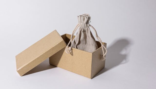 Flat lay of minimalist eco friendly packaging boxes and paper bags in neutral tones with subtle branding and natural props like leaves and linen