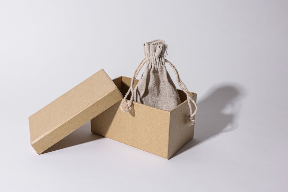 Flat lay of minimalist eco friendly packaging boxes and paper bags in neutral tones with subtle branding and natural props like leaves and linen